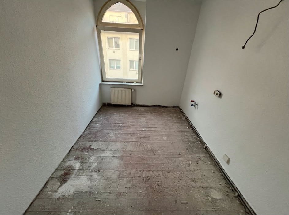 Bad vor der Sanierung: leerer Raum mit freigelegtem Boden und offenen Anschlüssen