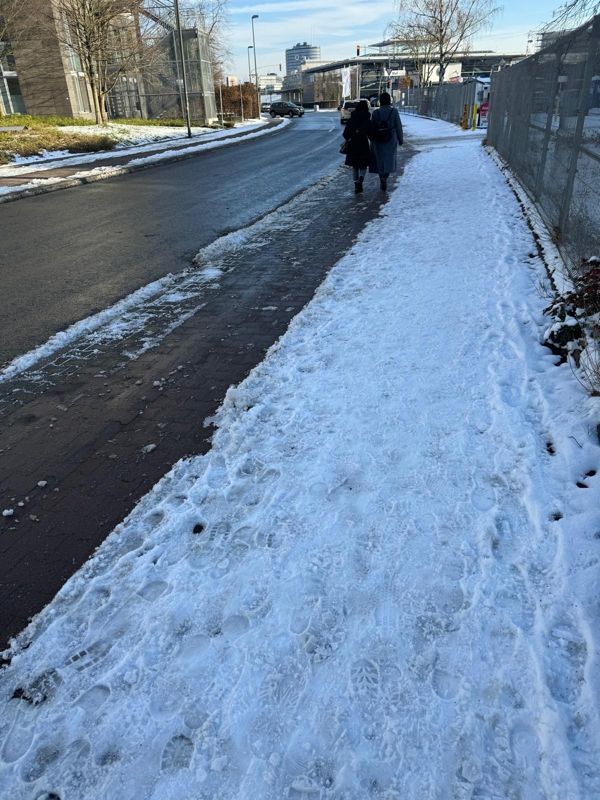Geräumter Gehweg im Winter, im Hintergrund Passanten auf dem Weg